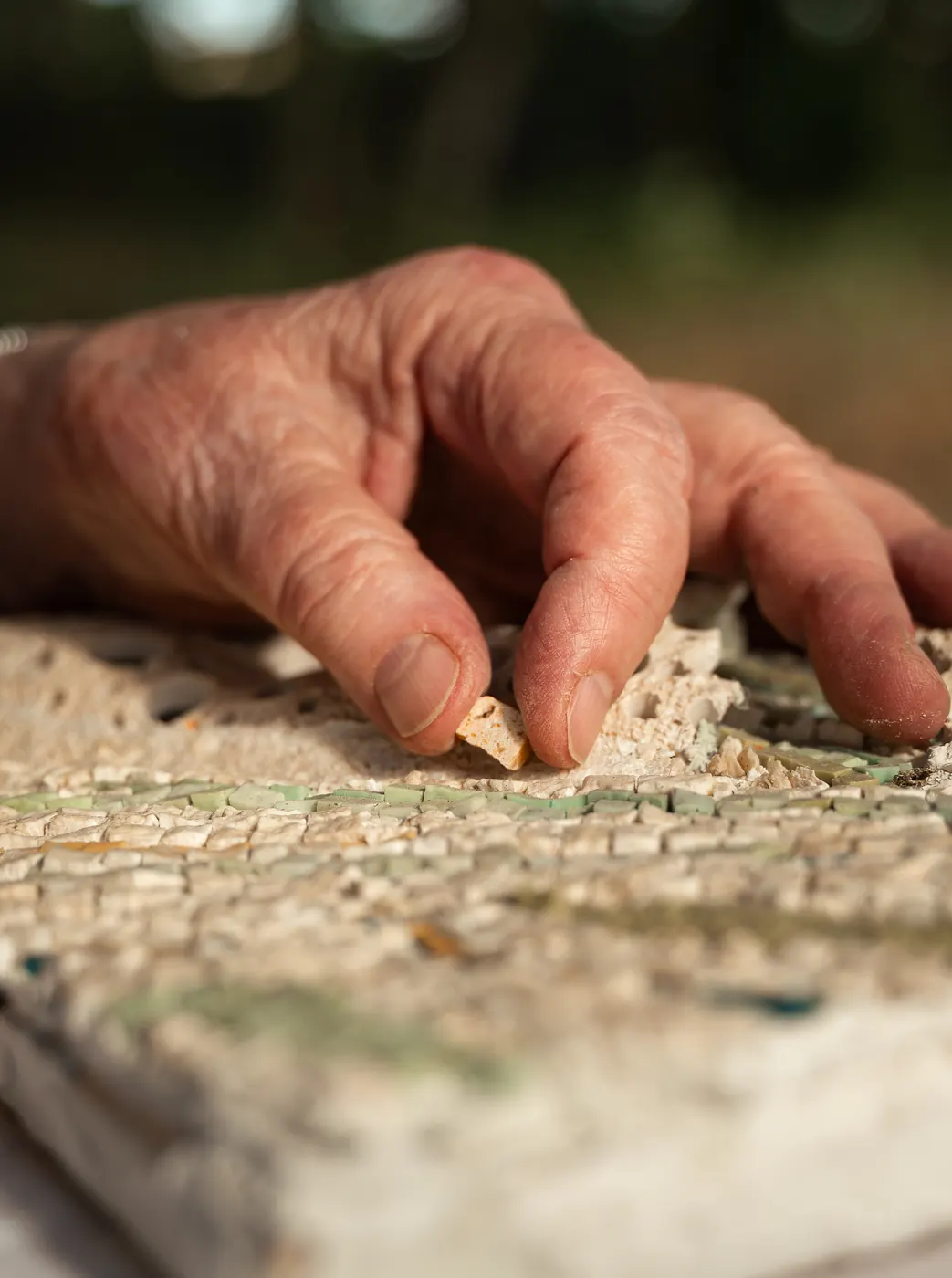 Les mains d'Anik-Chaïma posant une tesselle sur une mosaïque en cours
